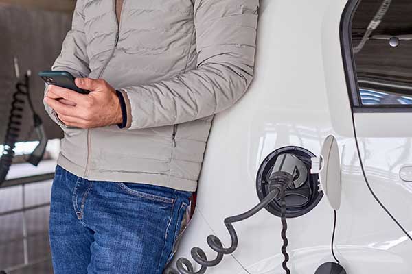 Man charging electric automobile and using his smartphone for payment at charging point